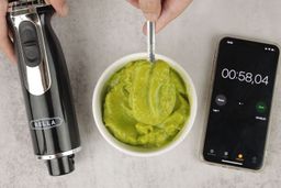 The BELLA 10-Speed Smoothie Testing, from left to right: the BELLA motor body, a batch of green smoothie in a white bowl with parts of it being scooped with a spoon, and a smartphone displaying the total blending time (58 seconds). 