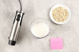 The KOIOS’s motor body, a plastic beaker containing almond milk, a white plate of almond pulp, and a small red note displaying the total grinding time (1 minute 30 seconds) being side by side. 