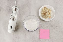 The UTALENT’s motor body, a plastic beaker containing almond milk, a white plate of almond pulp, and a small red note displaying the total grinding time (2 minutes) being side by side on a gray table. 