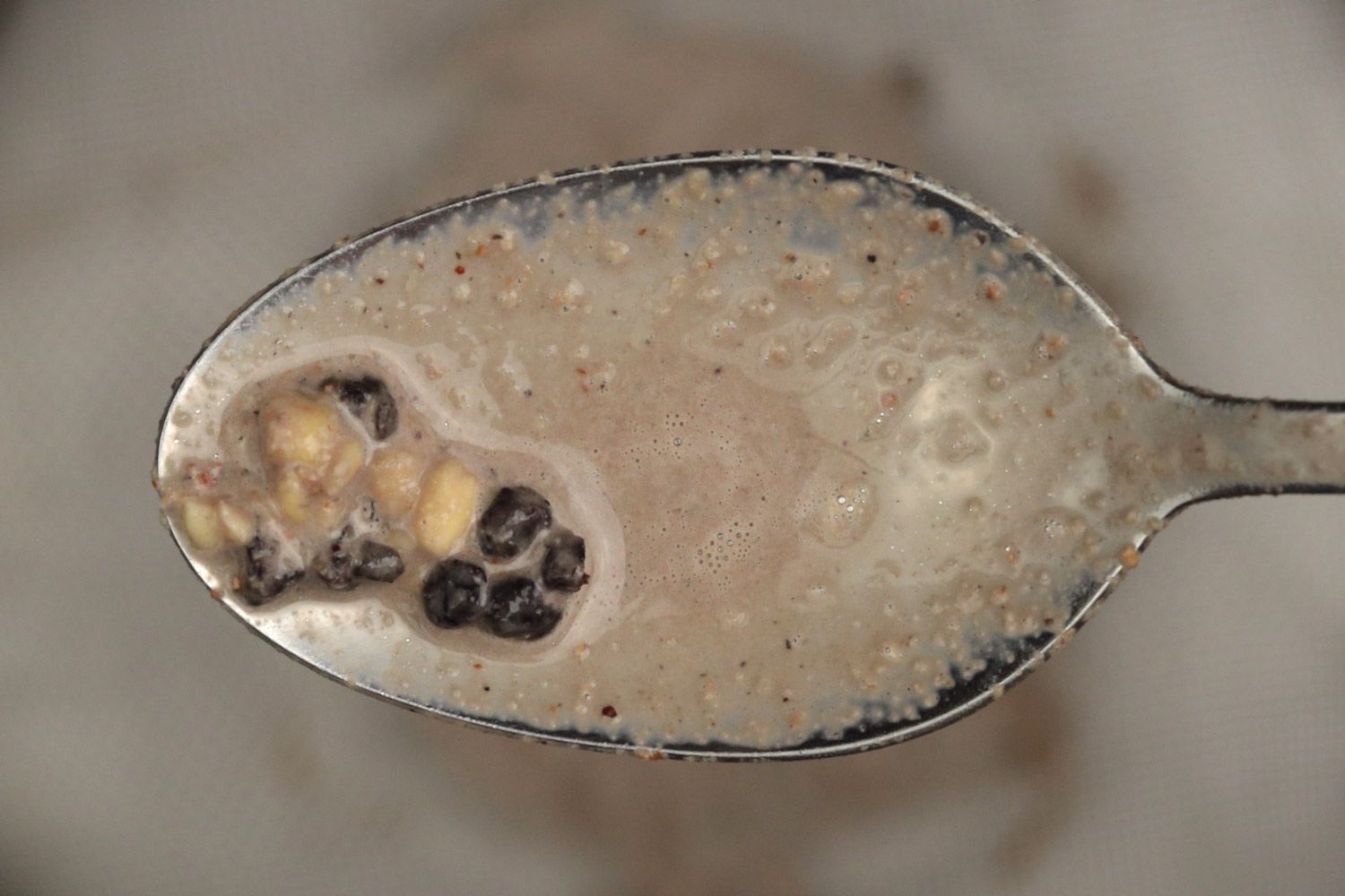 Using a spoon to remove a few unblended chunks, including almonds and dried blueberries, from a mesh strainer.