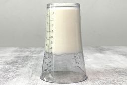 Putting a plastic beaker containing beaten egg-white of the Mueller Ultra-Stick upside down on a gray table.