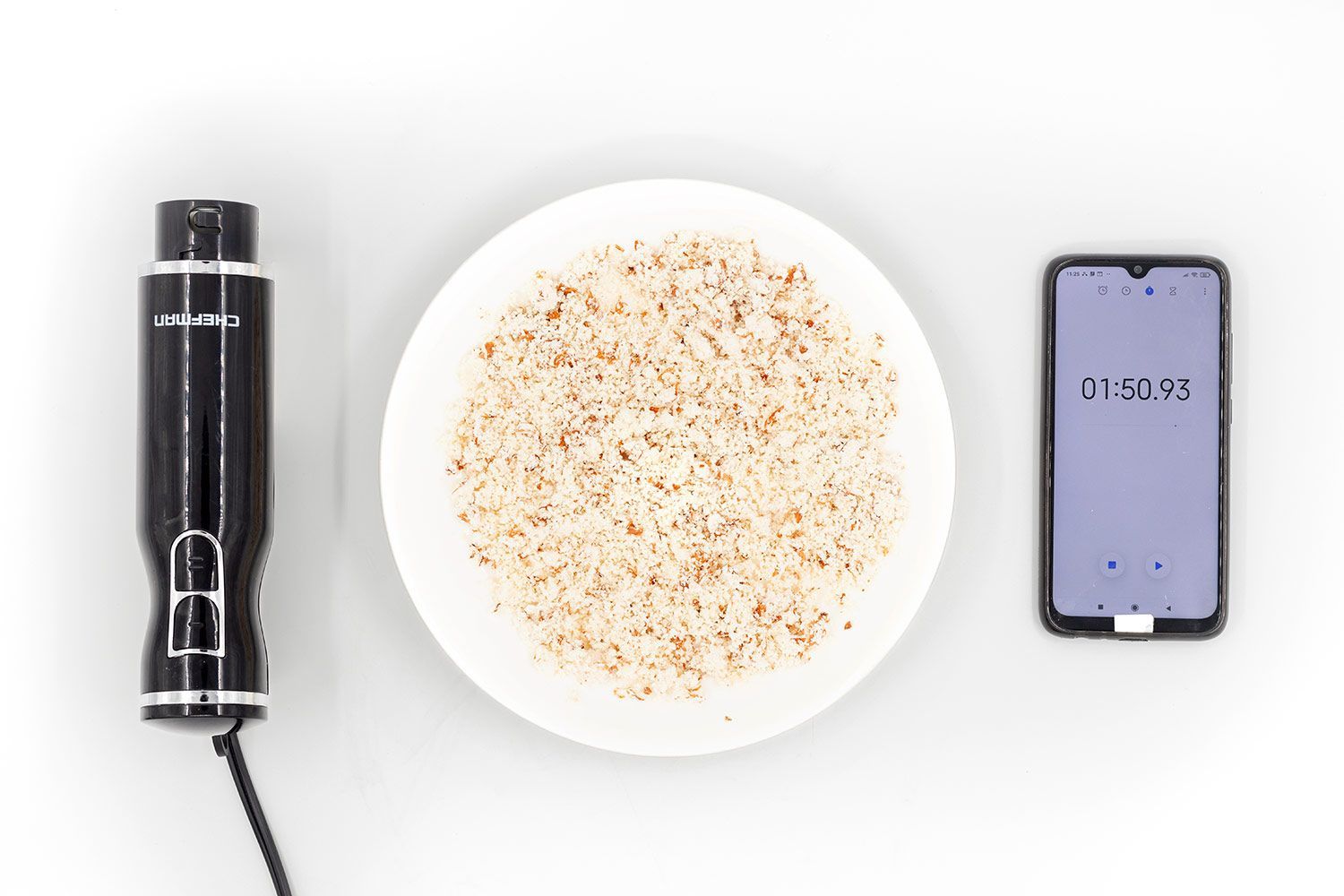 A white plate of almond pulp produced by the Chefman corded stick blender being between the Chefman’s motor body and a smartphone displaying the total grinding time (1 minute and 50 seconds).