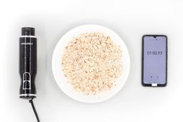 A white plate of almond pulp produced by the Chefman corded stick blender being between the Chefman’s motor body and a smartphone displaying the total grinding time (1 minute and 50 seconds).