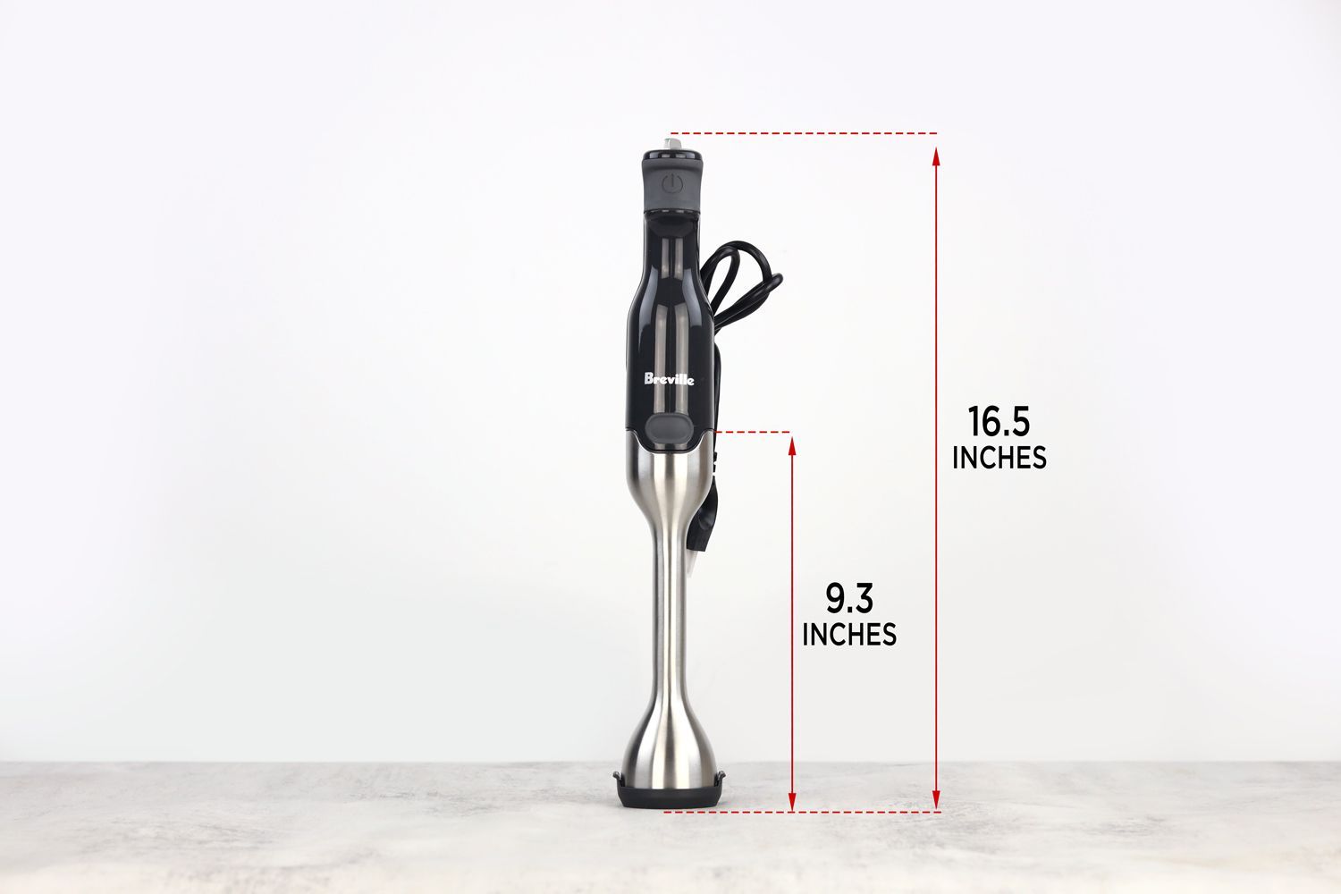 The Breville immersion blender standing on top of its blending shaft on a gray table, with the length of the blending shaft being noted to the side as 9.3 inches, and the total length of the unit as 16.5 inches. 