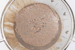 A mesh strainer filters a protein shake made by the NutriBullet, retaining the unblended solids that fail to pass through.