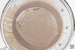 A mesh strainer filters a protein shake made by the Vitamix E310, retaining the unblended solids that fail to pass through.