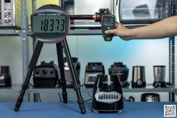 the Black+Decker blender motor base on table, hand pressing digital tachometer attached to tripod, different blenders in background.