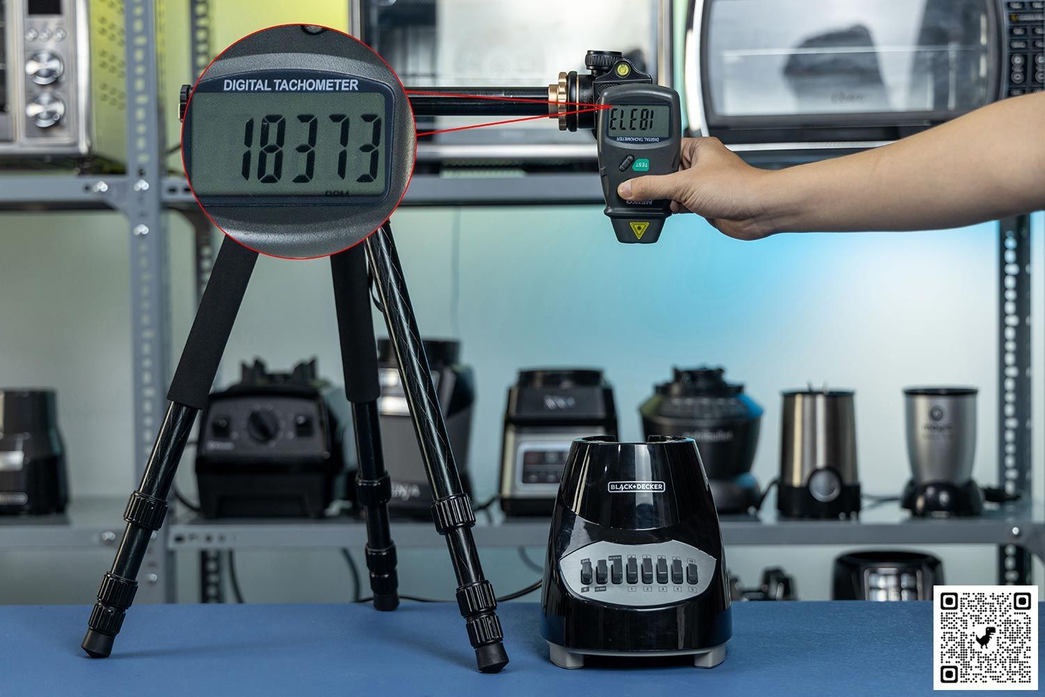 The Black+Decker Crush Master motor base on table with a hand pressing a digital tachometer on a tripod. Different blenders are visible in the background.