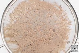 A mesh strainer filters a protein shake made by the Ninja AMZ493BRN, retaining the unblended solids that fail to pass through.