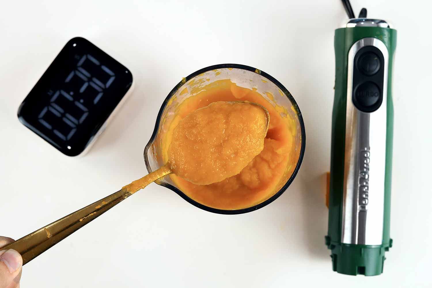 Scooping a spoon of pureéd soup produced by the Peach Street from the plastic beaker to check its smoothness.