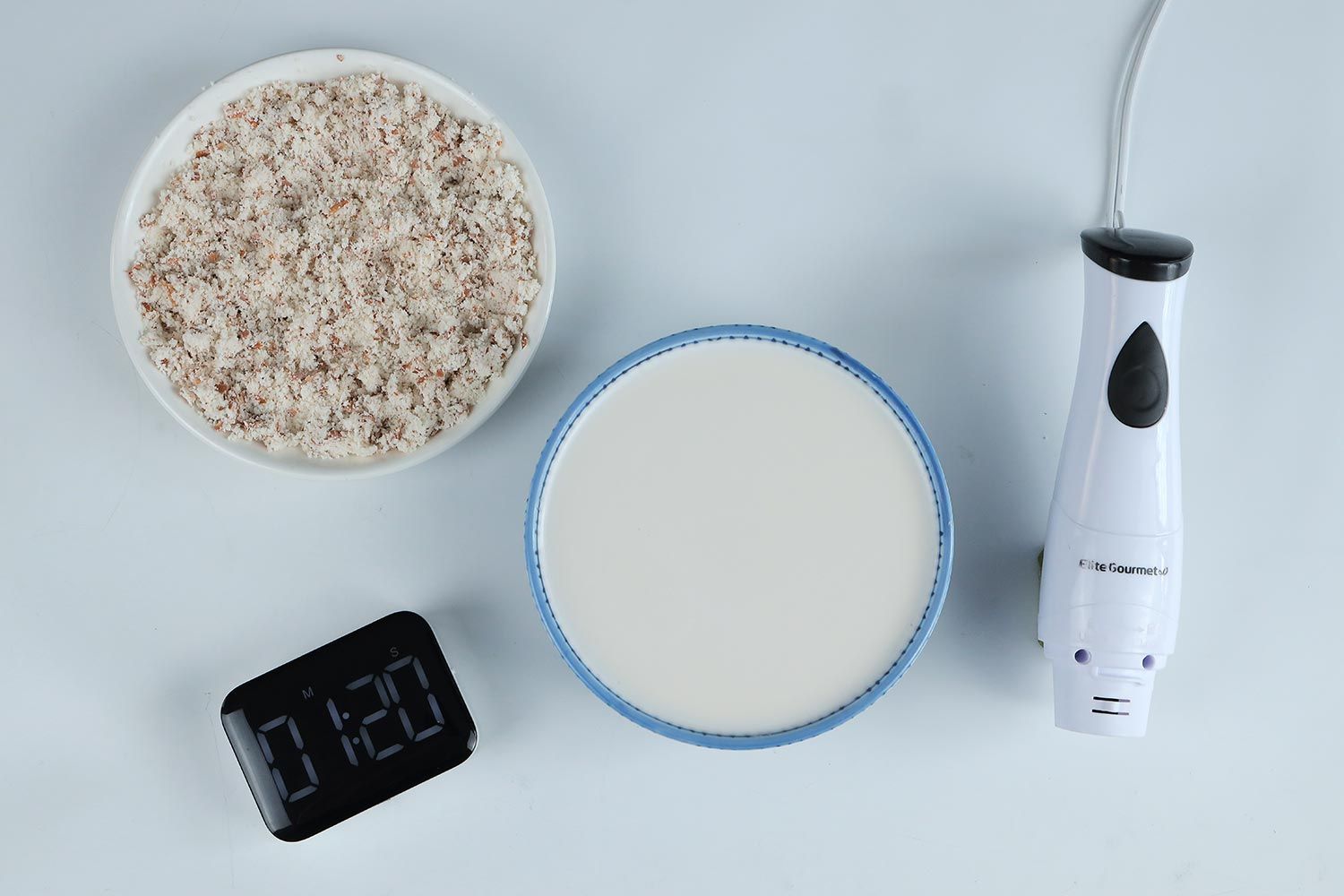 A white plate of almond pulp and a bowl of milk produced by the Elite Gourmet EHB-2425Xstick blender within 1 minute and 20 seconds.