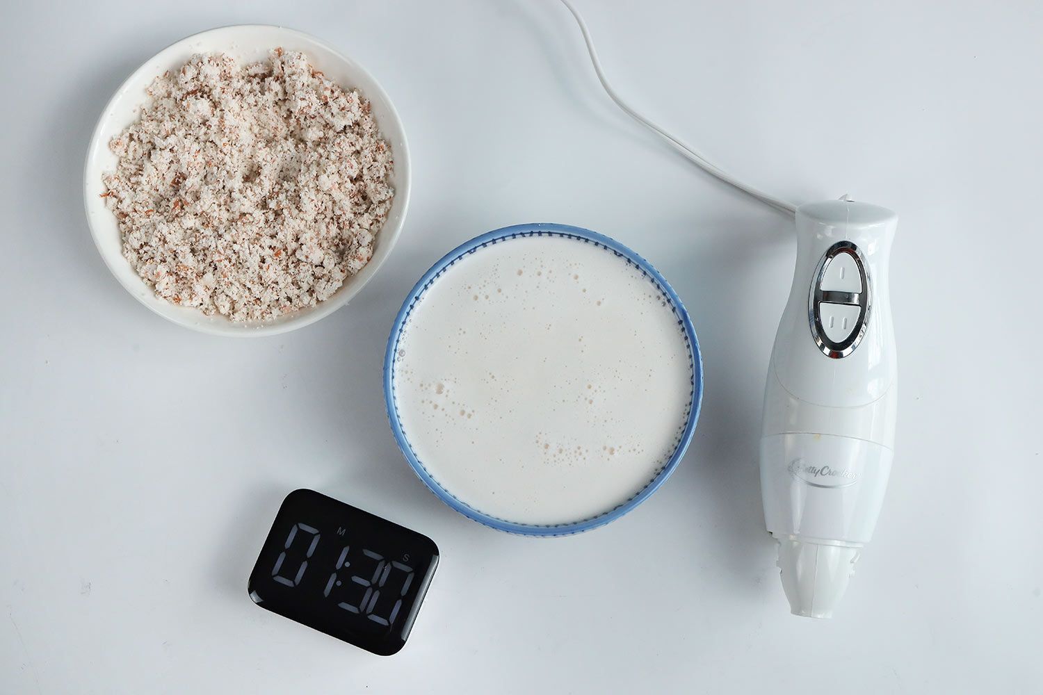 A white plate of almond pulp and a bowl of milk produced by the Betty Crocker stick blender within 1 minute and 30 seconds.