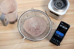 Protein shake test with the Ninja TWISTi, showing the shake poured through a fine mesh strainer after 1 minute to assess remaining grain and residue.