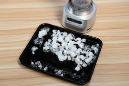 Ninja TWISTi ice crushing test, with finely crushed ice pieces spread on a black tray next to the blender base.