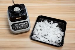 Ninja BL610 ice crushing test, with finely crushed ice pieces spread on a black tray next to the blender base.