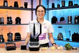 Tina conducts a smoothie test using banana, pineapple, apple, kale, and milk. She times the blend on her phone, and when the mixture stops moving efficiently, she pauses the blender and uses a spoon to push the ingredients back toward the blades for better circulation. After blending for three minutes, she spreads a spoonful on a sheet to check the texture up close and see how smooth it turns out.