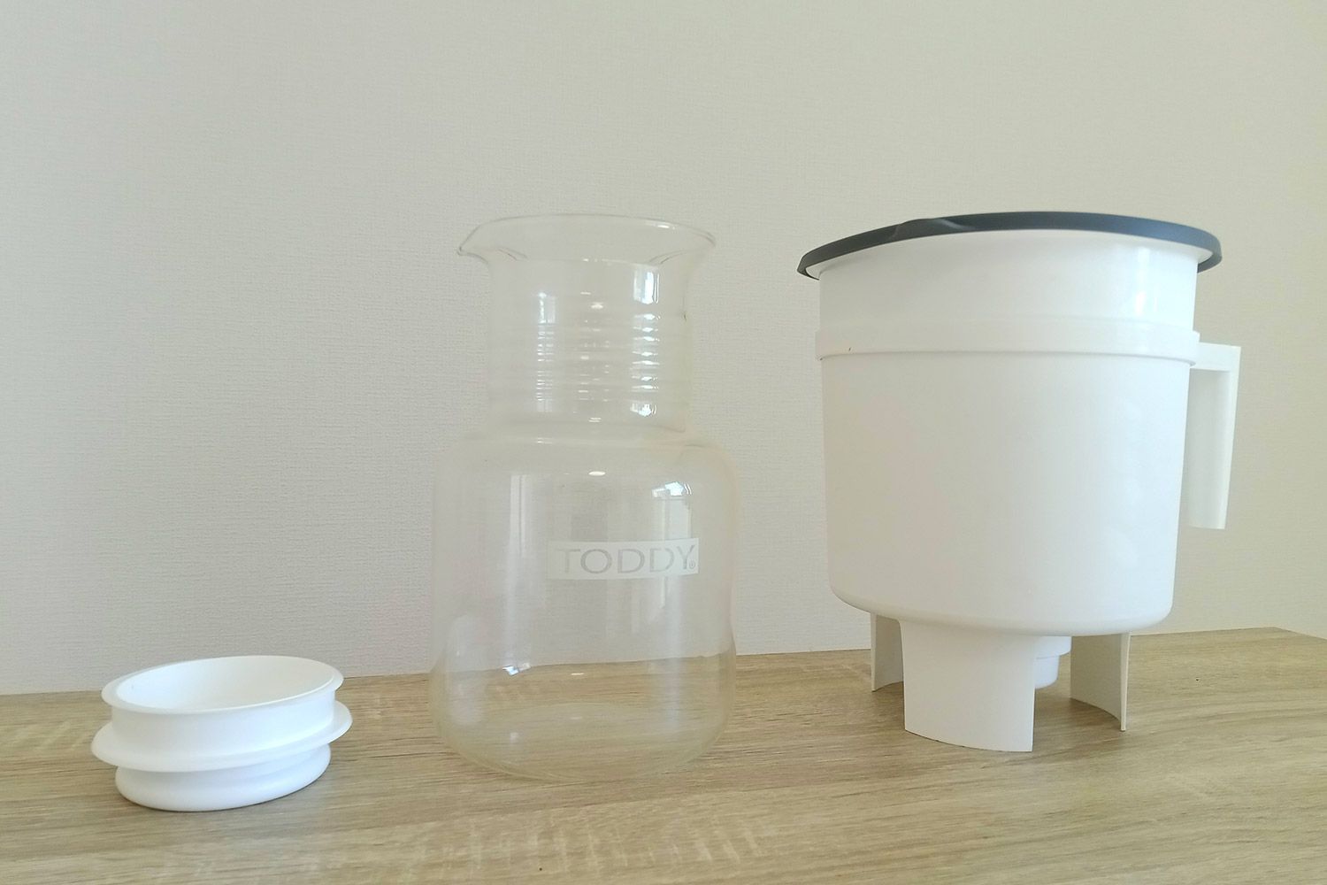 From left to right: The brew vessel, glass carafe, and silicone stopper of the Toddy Cold Brew System on a wooden counter.