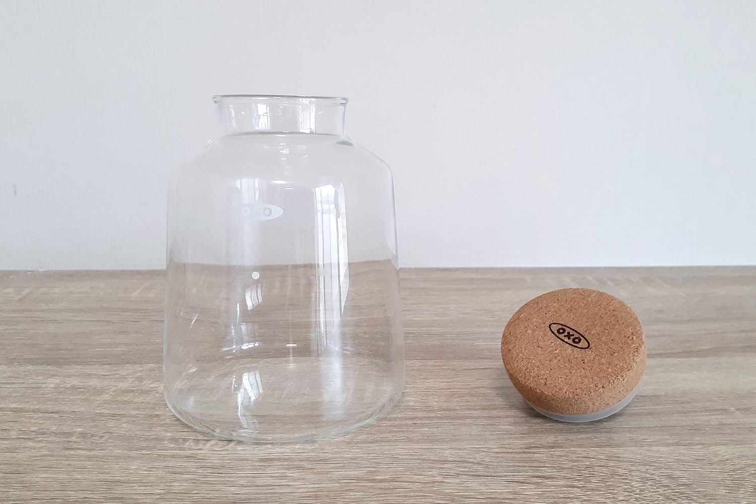 The small glass carafe of the Oxo compact cold brew coffee maker resting on a wood counter with the cork stopper to the right.