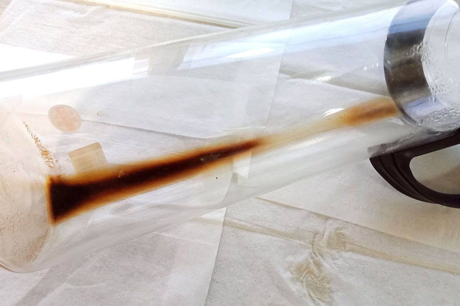 A close up view of sediment left over in a long glass brew carafe of a cold brew coffee maker. 