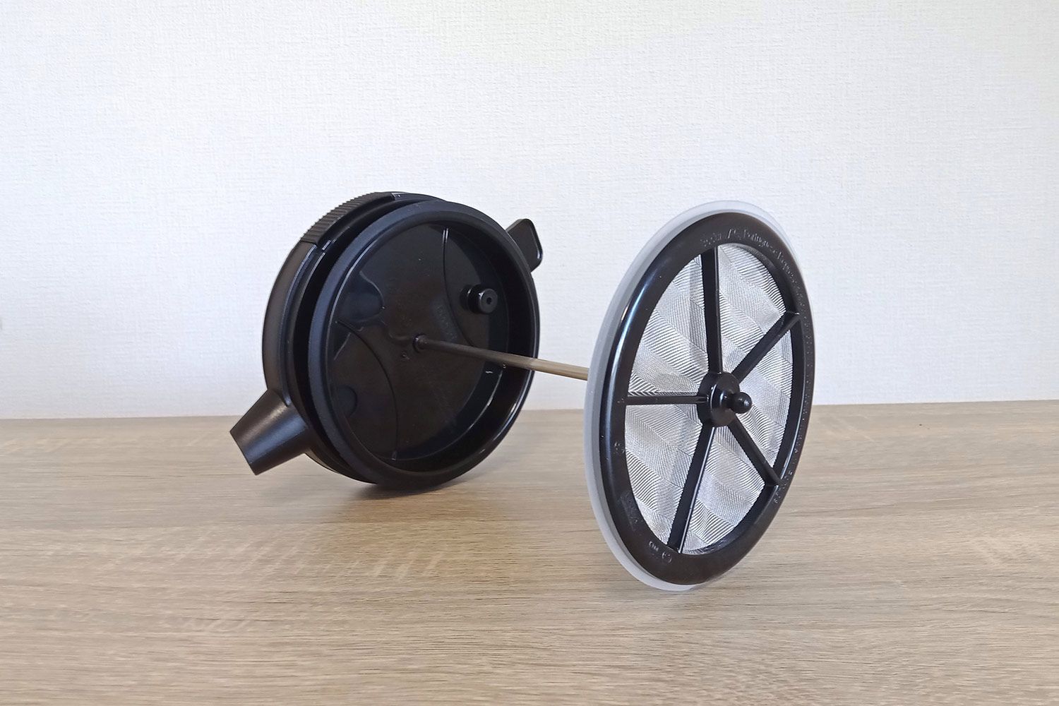 The plunge filter of the Bodum cold brew coffee maker with its attached lid lay sideways on a wooden counter.