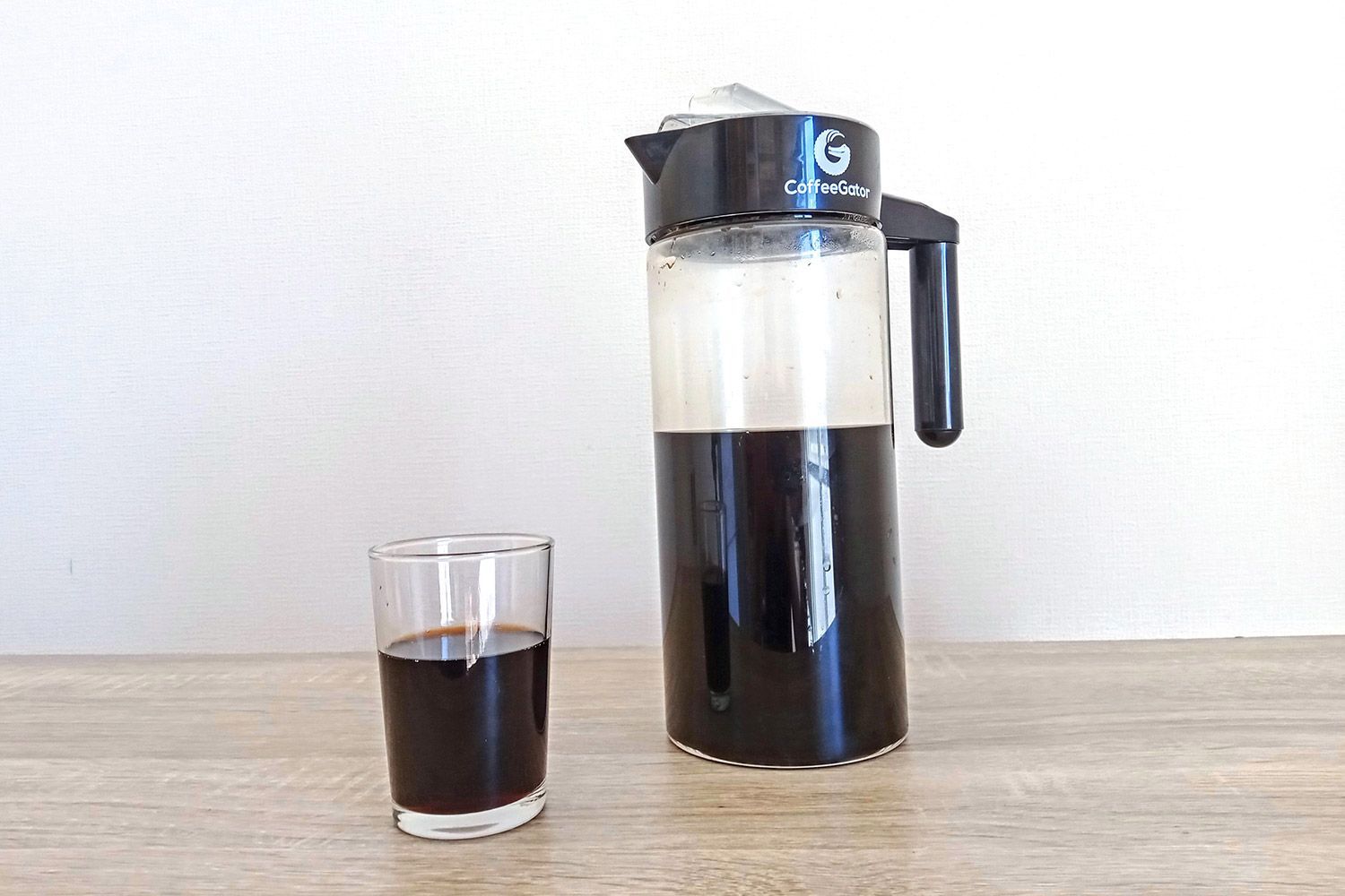 A small glass of coffee standing in the foreground and the Coffee Gator cold brew coffee jug-carafe in the background.