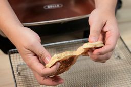 Two hands breaking a pancake apart. In the background is the Bella Non-Stick Electric Skillet 14607.