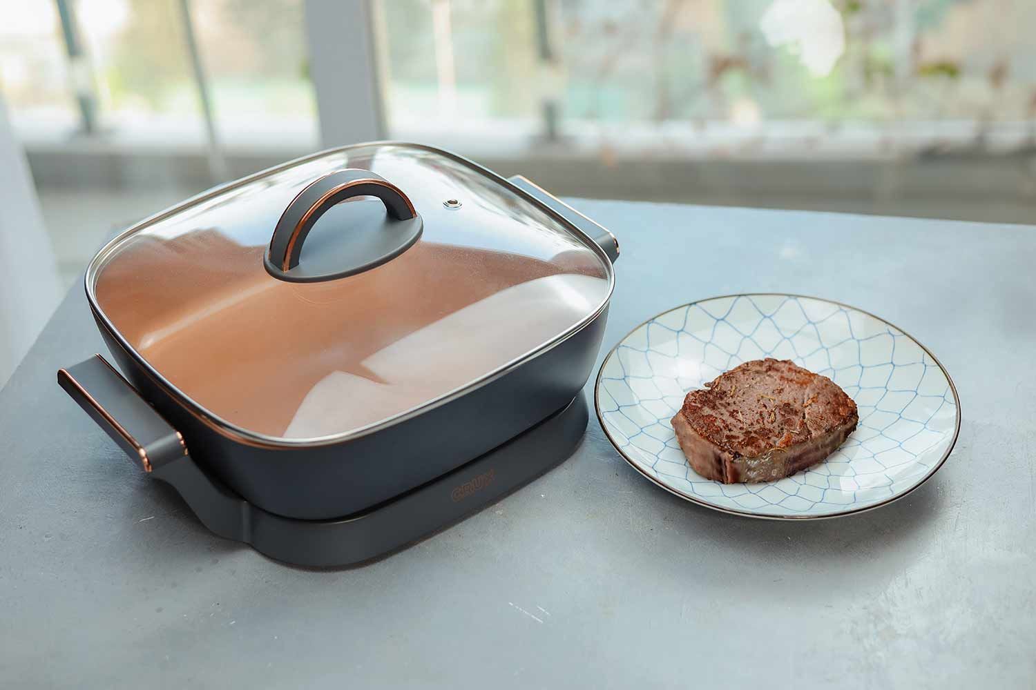 The CRUX Electric Skillet 14620  on the left and a plate of steak made with it on the right.