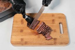 On the cutting board, a tong is holding the steak while a knife is slicing the steak.