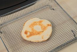 The bottom side of a golden brown pancake that’s dark around the edges inside an air fryer basket. In the corner is the Crux Non-Stick Electric Skillet 14620.