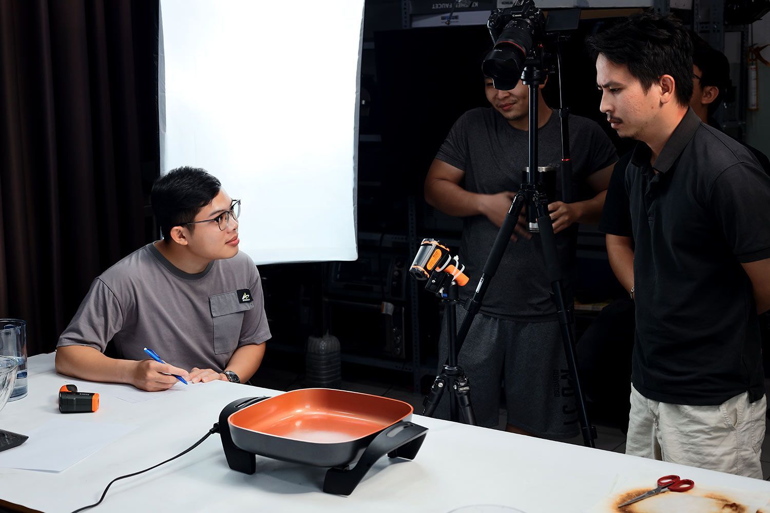 A camera, an infrared thermometer, an electric skillet, and four people discussing.