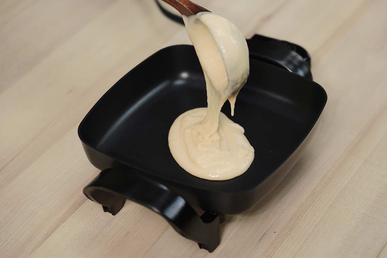 Pouring batter into the Nesco Non-Stick Electric Skillet ES-08 with a scoop.