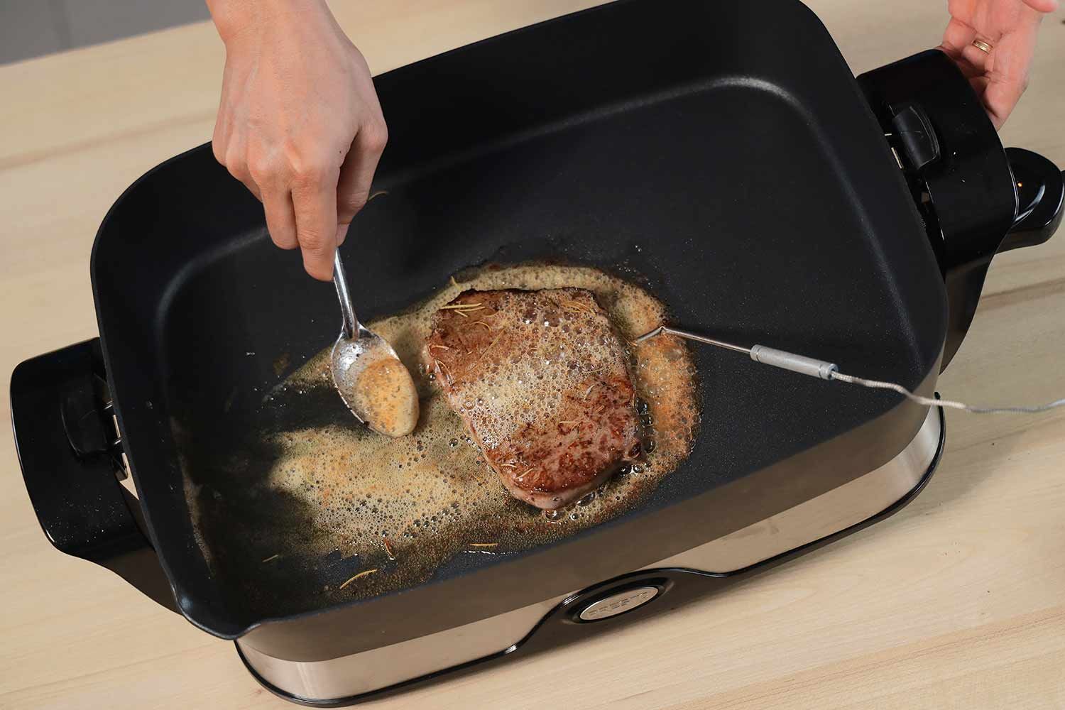 Coating a steak with butter inside the Presto Foldaway Non-Stick Electric Skillet 06857.