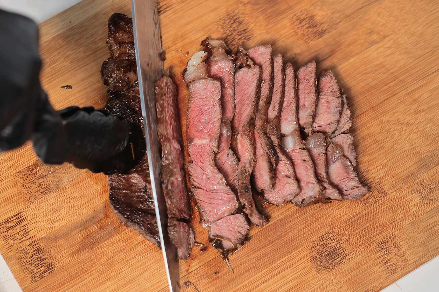 Slicing up a steak on a wooden cutting board.