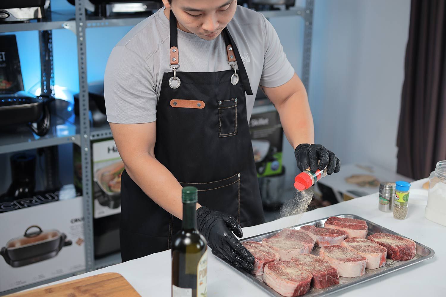 A person in an apron seasoning a tray of steak with garlic powder.