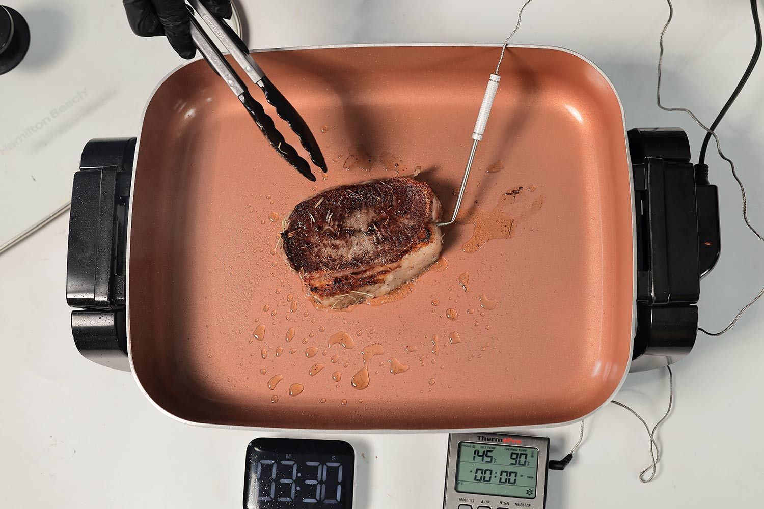 Searing a steak using the Hamilton Beach Ceramic Non-Stick Electric Skillet 38529K. A digital timer, and a meat thermometer.