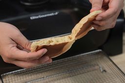 Two hands breaking a pancake apart. In the background is the Elite Gourmet Non-Stick Electric Skillet EG-6203.