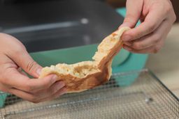 Two hands breaking a pancake apart. In the background is the GreenLife Ceramic Non-Stick Electric Skillet CC003725-002.