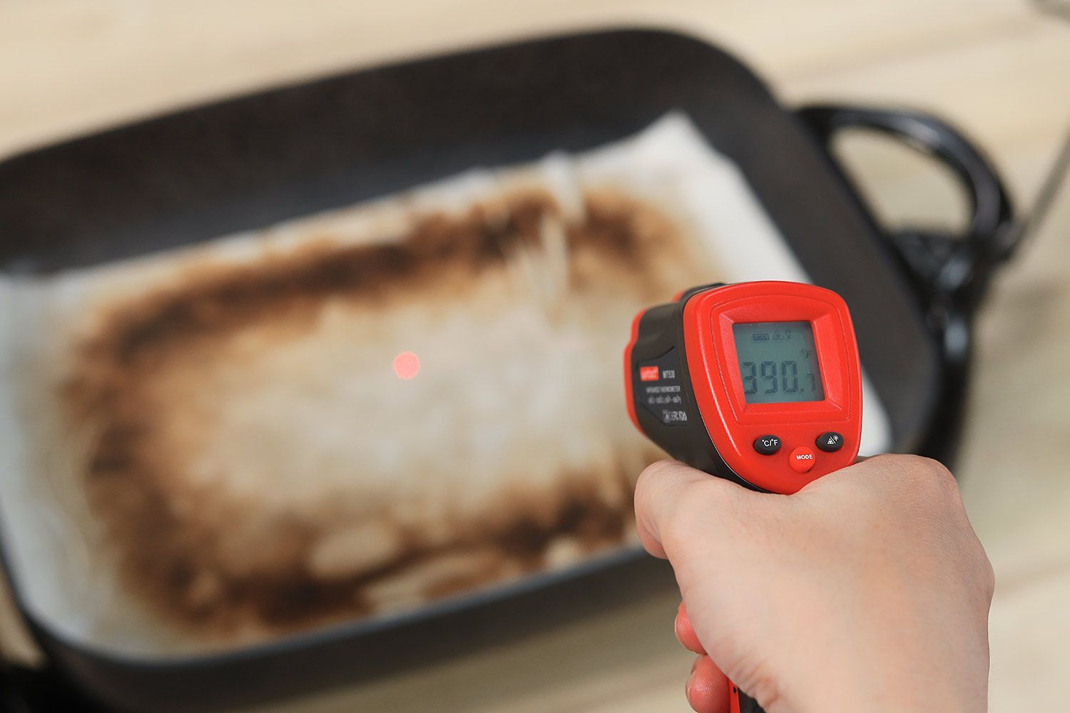 An oil absorbent sheet with dark caramelized rectangles laid on a skillet’s surface. An infrared thermometer reads 390°F.