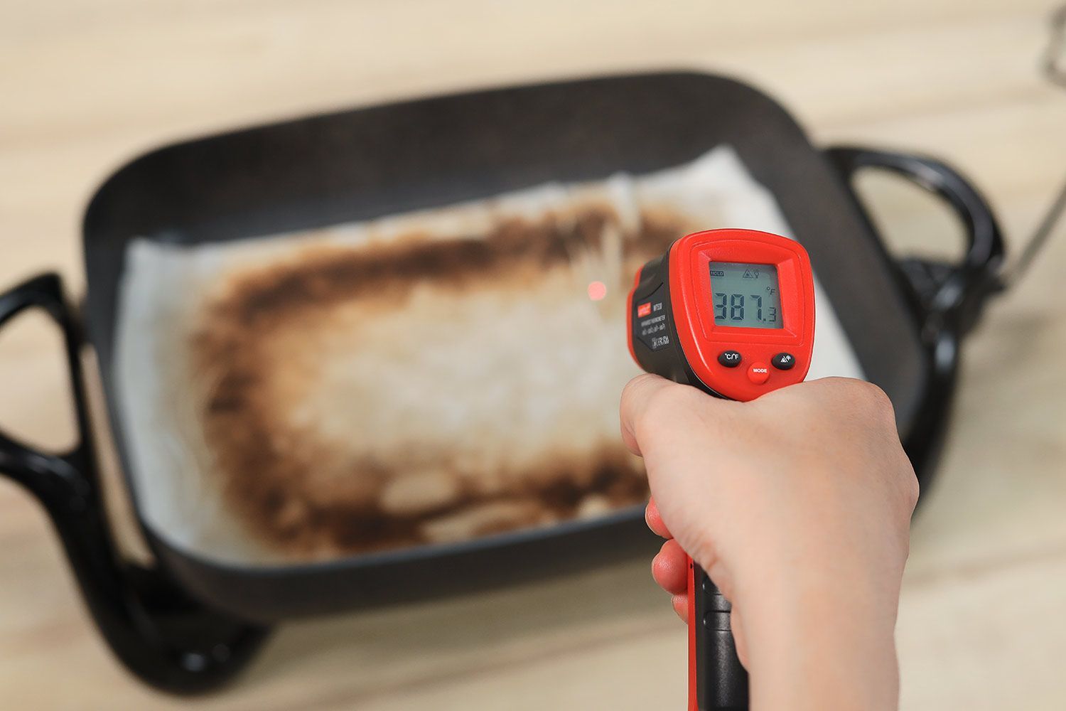 An oil absorbent sheet with dark caramelized rectangles laid on a skillet’s surface. An infrared thermometer reads 387°F.