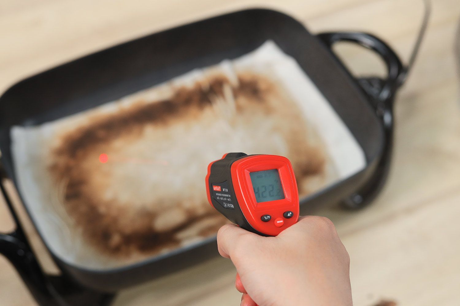 An oil absorbent sheet with dark caramelized rectangles laid on a skillet’s surface. An infrared thermometer reads 422°F.