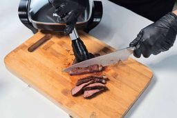 On the cutting board, a tong is holding the steak while a knife is slicing the steak.