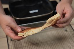 Two hands breaking a pancake apart. In the background is the Nesco Non-Stick Electric Skillet ES-08.