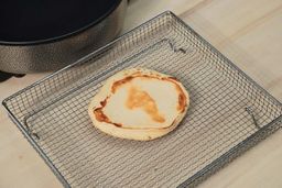 The bottom side of a golden brown pancake that’s dark around the edges inside an air fryer basket. In the corner is the Ovente Non-Stick Electric Skillet SK11112B.