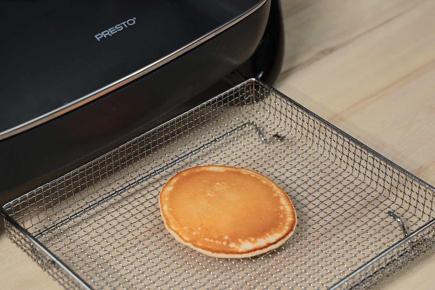 The top side of a golden brown pancake inside an air fryer basket. In the corner is the Presto Electric Skillet 06852.