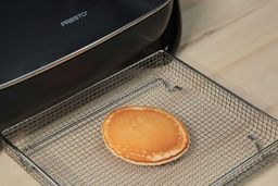 The top side of a golden brown pancake inside an air fryer basket. In the corner is the Presto Electric Skillet 06852.