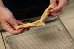 Two hands breaking a pancake apart. In the background is the Presto Foldaway Non-Stick Electric Skillet 06857.