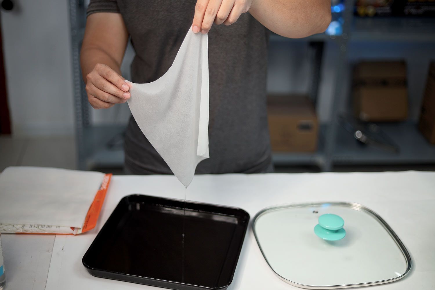 Two hands lifting up an oil absorbent sheet soaked in sugar water.