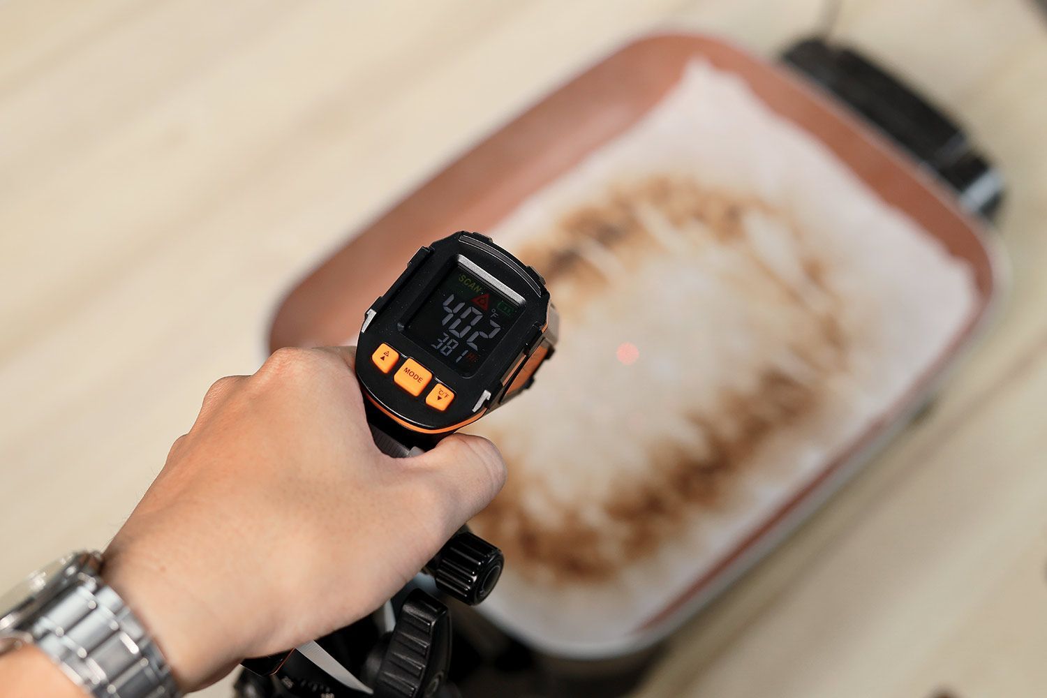 An oil absorbent sheet with dark caramelized rectangles laid on a skillet’s surface. An infrared thermometer reads 402°F.