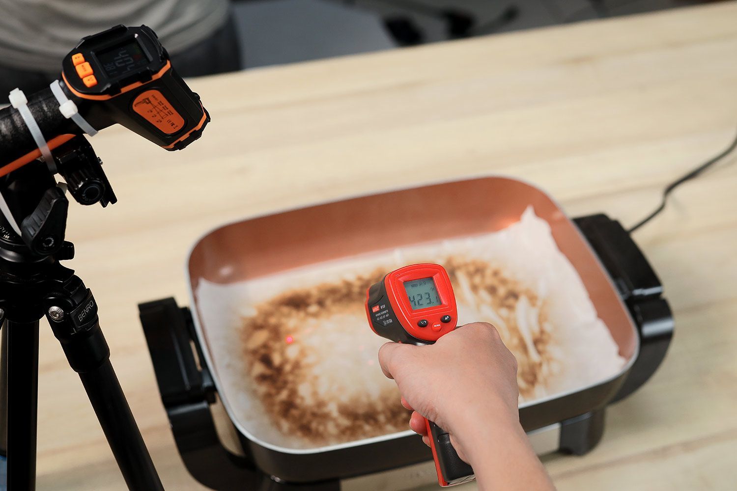 An oil absorbent sheet with dark caramelized rectangles laid on a skillet’s surface. An infrared thermometer reads 423°F.