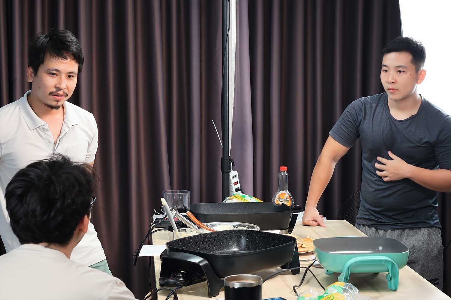 Three people discussing electric skillets. Also on the table are testing equipment and ingredients.